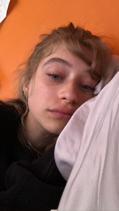 a woman laying on top of a bed next to an orange wall