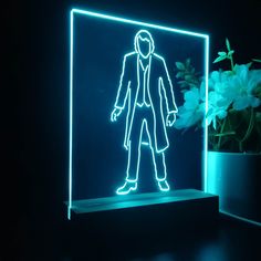 a neon sign with a man standing in front of it on a black surface next to a potted plant