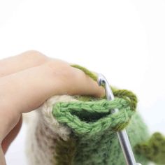 someone is crocheting the ends of a green piece of yarn with a pair of scissors