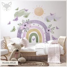 a teddy bear sitting on top of a bed next to a rainbow wall decal