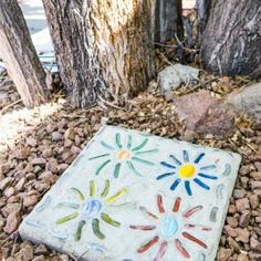 a painted tile sitting on the ground next to some trees and rocks in front of a tree