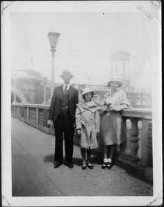 an old black and white photo of three people standing on a bridge near a lamp post