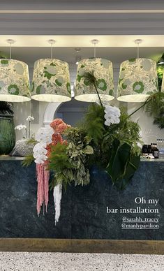 a counter with flowers and plants on it in front of some lamps hanging from the ceiling