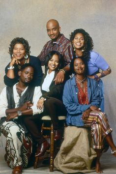 a group of people sitting next to each other in front of a gray background with one person smiling at the camera