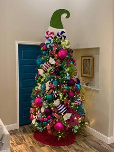 a decorated christmas tree in the corner of a room with blue door and green hat on top