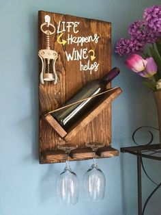 a wooden wine rack with two wine glasses hanging from it's side and a vase filled with purple flowers in the background