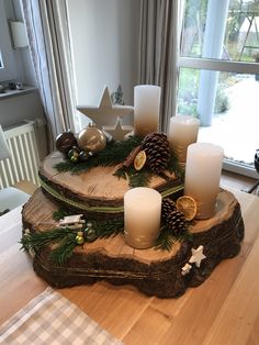 a wooden table topped with candles next to a christmas tree branch covered in pine cones