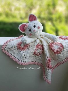 a crocheted white and pink teddy bear on top of a blanket with flowers