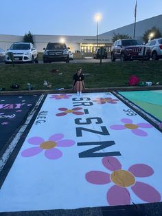 a woman sitting on the ground in front of a parking lot with flowers painted on it