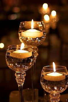 three wine glasses sitting on top of a table next to each other with candles in them