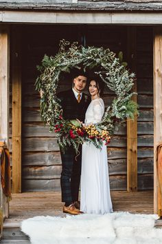 a man and woman standing in front of a wooden building with a wreath on it