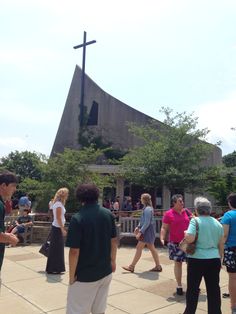 people are walking around in front of a church with a cross on the top of it