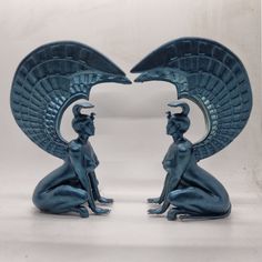 two blue statues sitting next to each other on top of a white surface with wings