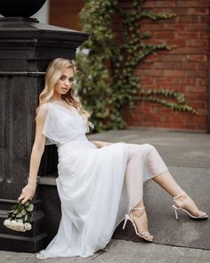 a woman sitting on the side of a street next to a lamp post holding a bouquet