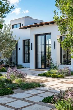 a white house with lots of plants and trees in front of the door, surrounded by stone walkways