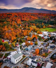 an aerial view of a small town surrounded by trees with fall foliage in the background