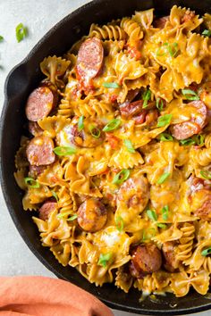 a skillet filled with pasta, sausages and cheese on top of a table