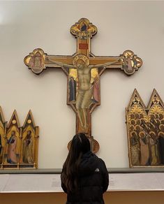 a woman standing in front of a cross with paintings on the wall behind her,