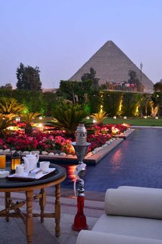 an outdoor dining area next to a pool and pyramids in the background at dusk