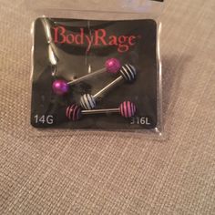 a package of body rage piercings with pink and black balls on them sitting on a bed