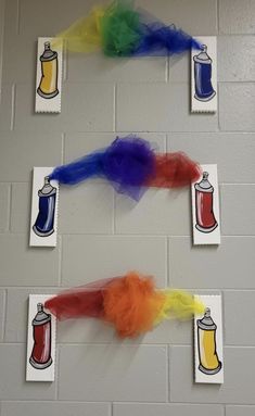 three different colored objects are hanging on the wall in front of two pictures that have been made to look like soda cans