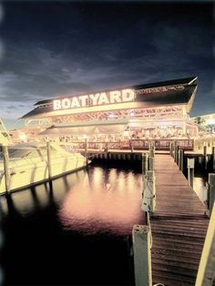 the boatyard is lit up at night with lights on it's roof and water below