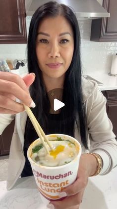 a woman holding a bowl of food with chopsticks in her hand