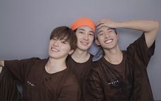 three young men are posing for the camera with their hands on their head and one is wearing an orange beanie