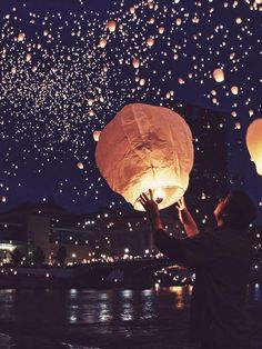 a man is releasing lanterns into the air at night with lights in the sky above him