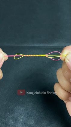 two hands are holding a string that is pink and yellow, while another hand holds the string in front of them