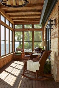 a porch with rocking chairs and windows overlooking the water is shown in this photo from inside