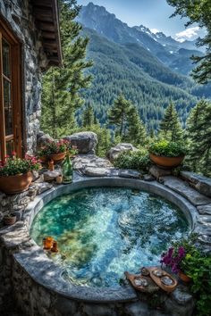 an outdoor hot tub surrounded by plants and flowers in front of a stone building with mountains in the background