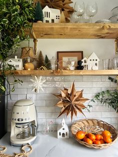 a kitchen counter topped with oranges next to a blender and shelves filled with christmas decorations