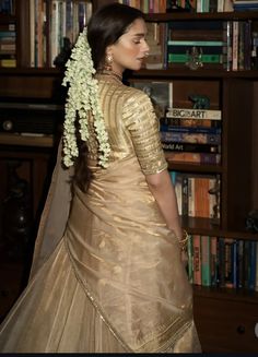 a woman standing in front of a bookshelf wearing a gold and white lehenga