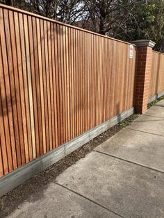 a wooden fence next to a sidewalk and trees