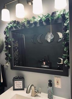 a bathroom with a sink, mirror and lights on the wall above it is decorated with greenery