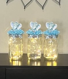 three mason jars with lights in them are sitting on a table next to a wall