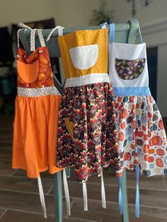 three aprons hanging from clothes racks on the floor