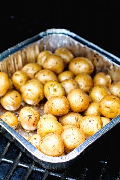 some potatoes are sitting in an aluminum pan on the grill, ready to be cooked