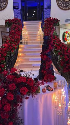 a table with candles and flowers on it in front of a staircase decorated with red roses