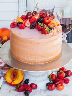 a cake with berries and peaches on top sitting on a table next to other fruit