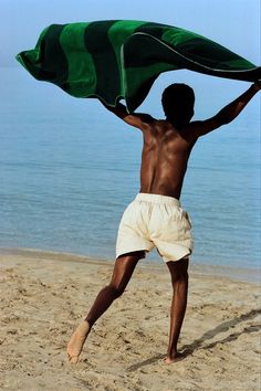 a man is standing on the beach with a towel over his head and hands in the air