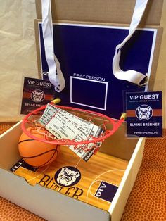 an open box containing a basketball, ticket cards and lanyard tag with a white ribbon