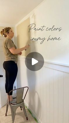 a woman is painting the wall in her house with white paint and she is standing on a chair