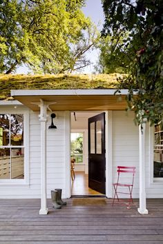 a white house with a green roof and two chairs on the front porch, next to an open door