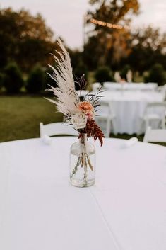 a vase filled with flowers and feathers on top of a white tablecloth covered field