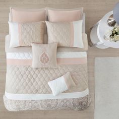 a bed with pink and white comforters on top of it next to a table