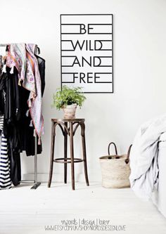 a bedroom with clothes hanging on the wall and a bed next to it in front of a poster that says be wild and free