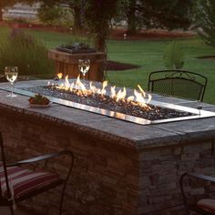 an outdoor fire pit with wine glasses on it and two chairs around the firepit