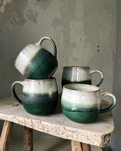 three green and white ceramic cups sitting on top of a wooden table next to a wall